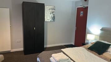 Hotelkamer met een zwarte garderobe, een bed met een wit en groen kussen, een rode deur en een kunstwerk aan de muur.
