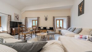 Een ruime woonkamer met een bank, stoelen, een klein rond tafeltje en een televisie.