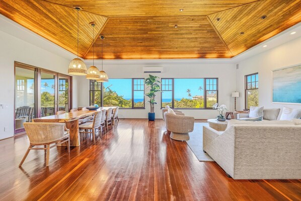 A spacious room with a wooden ceiling, large windows, a dining area, and a seating area.