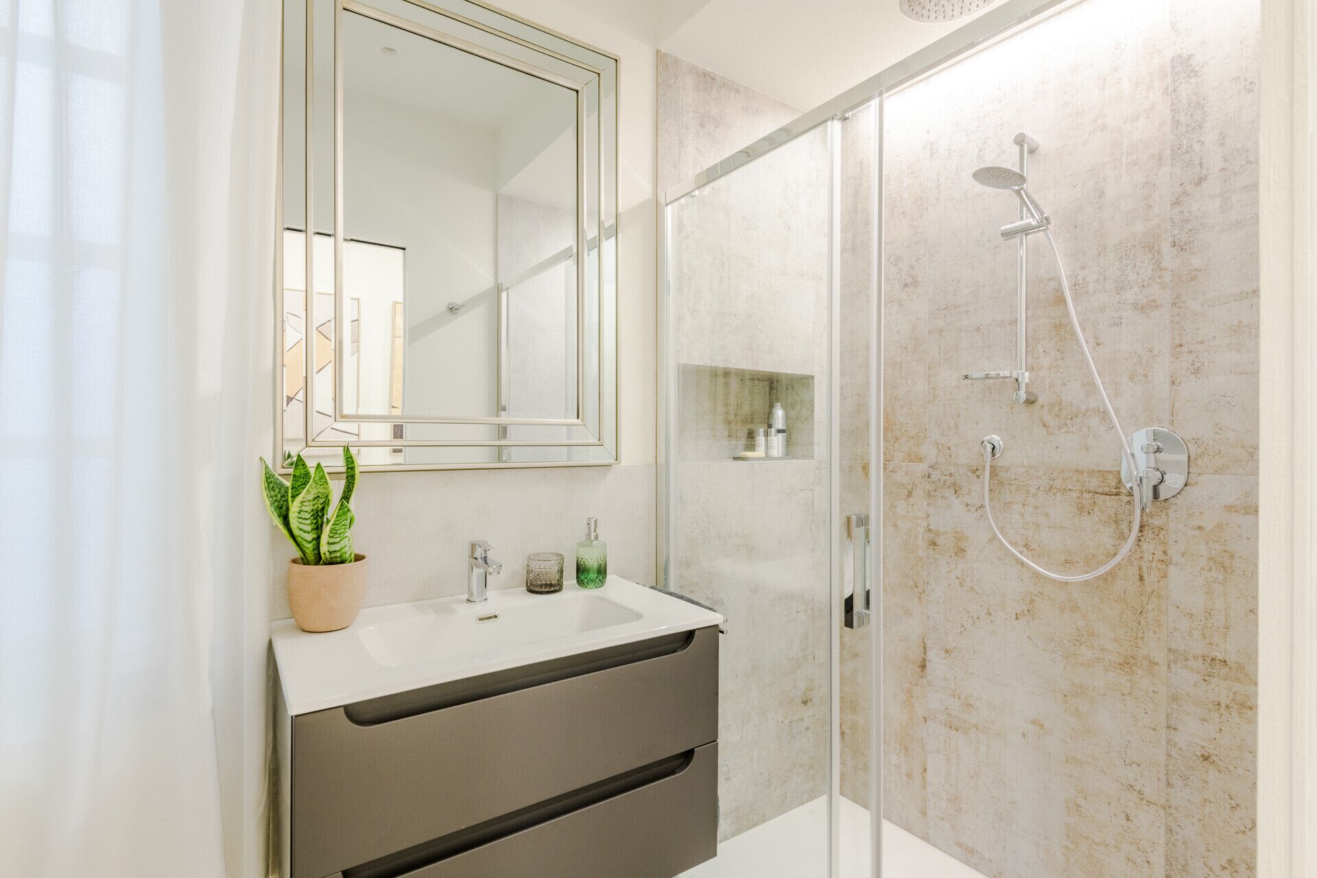 Une salle de bain moderne avec une douche en verre, un lavabo surmonté d’un miroir et une plante en pot.