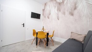 Een moderne kamer met een eettafel, gele stoelen, een grijze bank en een aan de muur bevestigde televisie.
