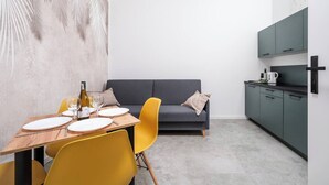 Een moderne keuken met grijze kastjes, een eettafel met gele stoelen en een grijze bank.