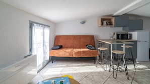 A compact living space with a sofa, a small kitchen area, and a dining table with stools. - Le Nid de Pézenas - Centre de Pézenas (Pézenas)