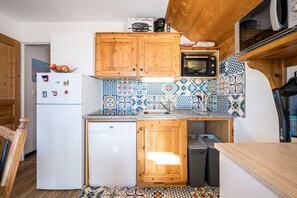 Une cuisine compacte avec des meubles en bois, un four à micro-ondes, un lave-vaisselle et un dosseret carrelé.