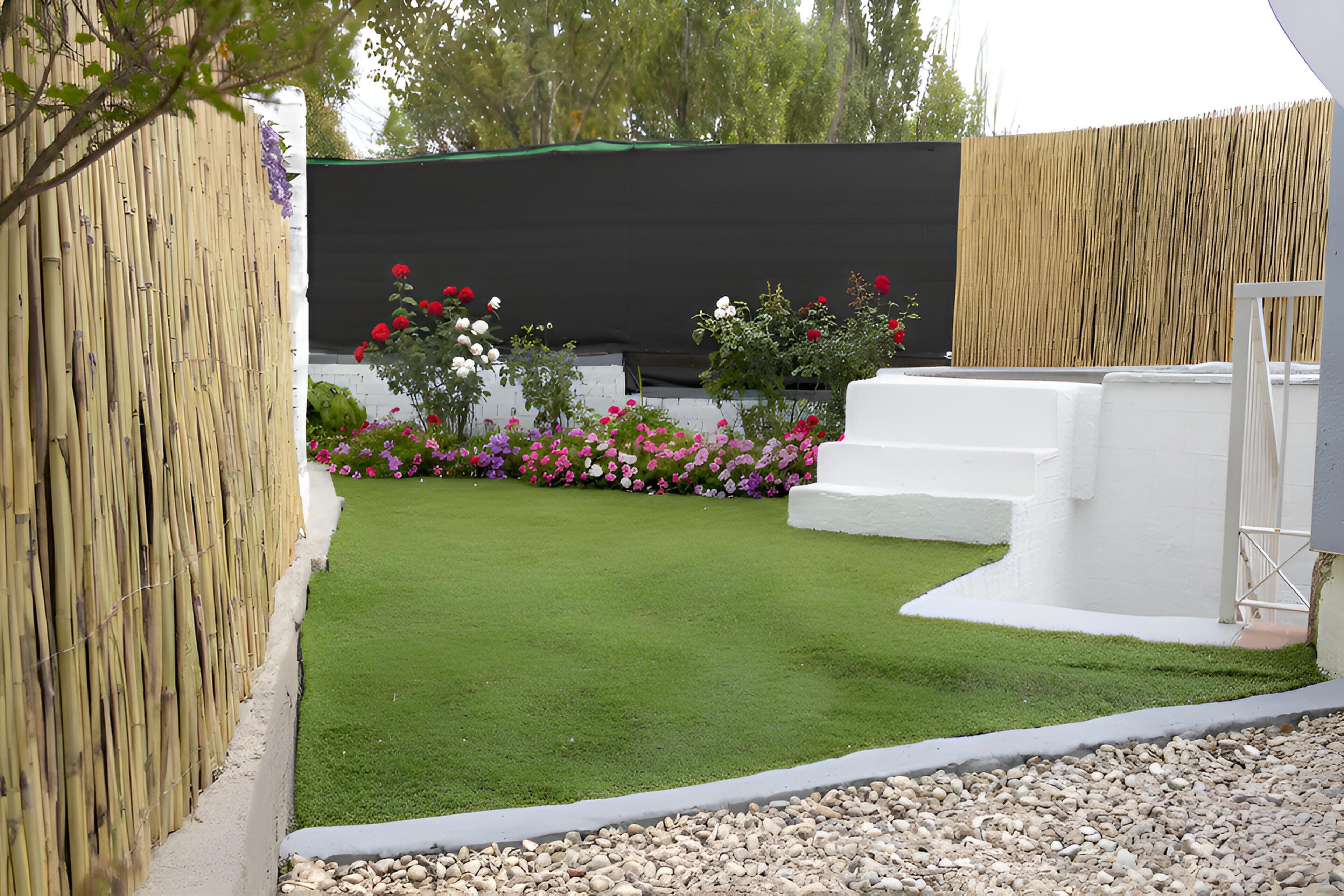 Een verzorgde tuin met een groen gazon, diverse bloemen en een witte constructie.