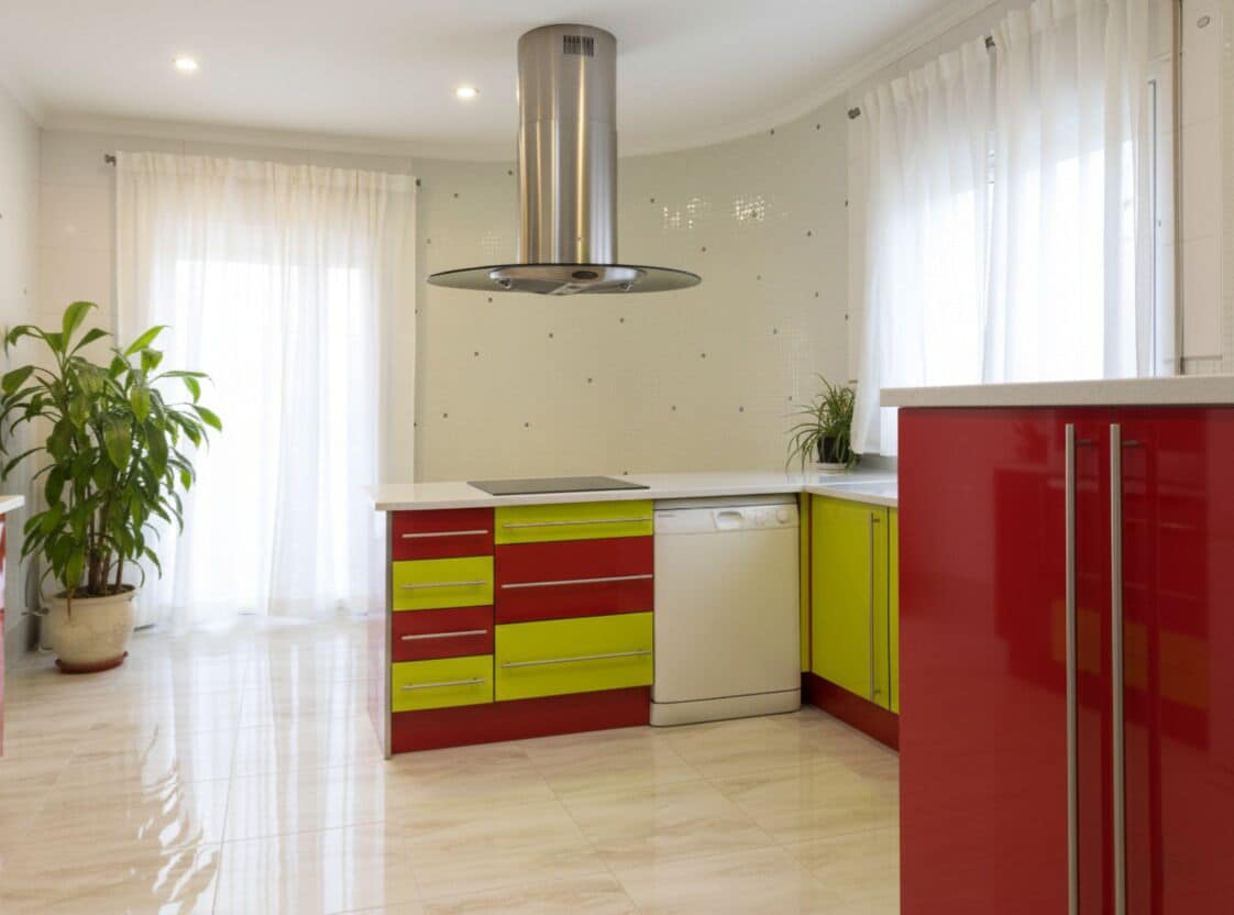 Una cocina moderna con una isla central, lavavajillas empotrado y una campana extractora de acero inoxidable. Hay plantas en macetas y un ventanal con cortinas.