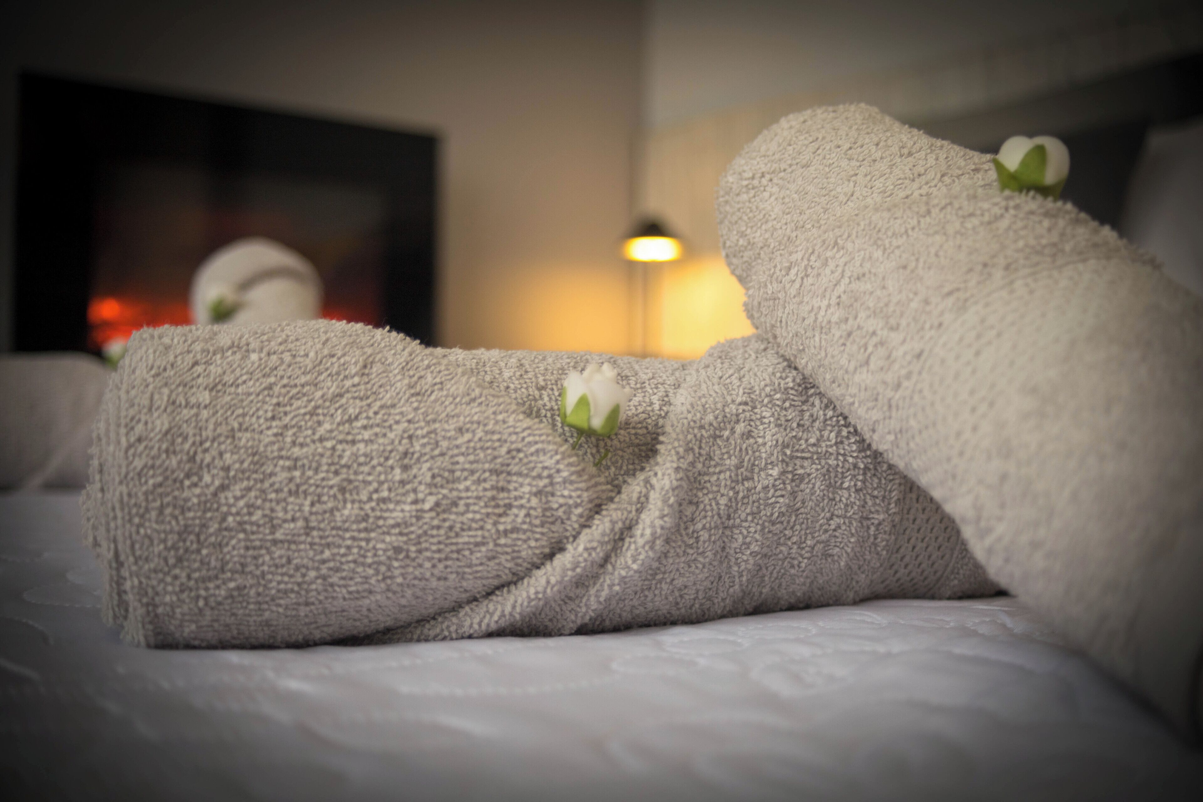 A neatly made bed with a white towel and a small white flower.