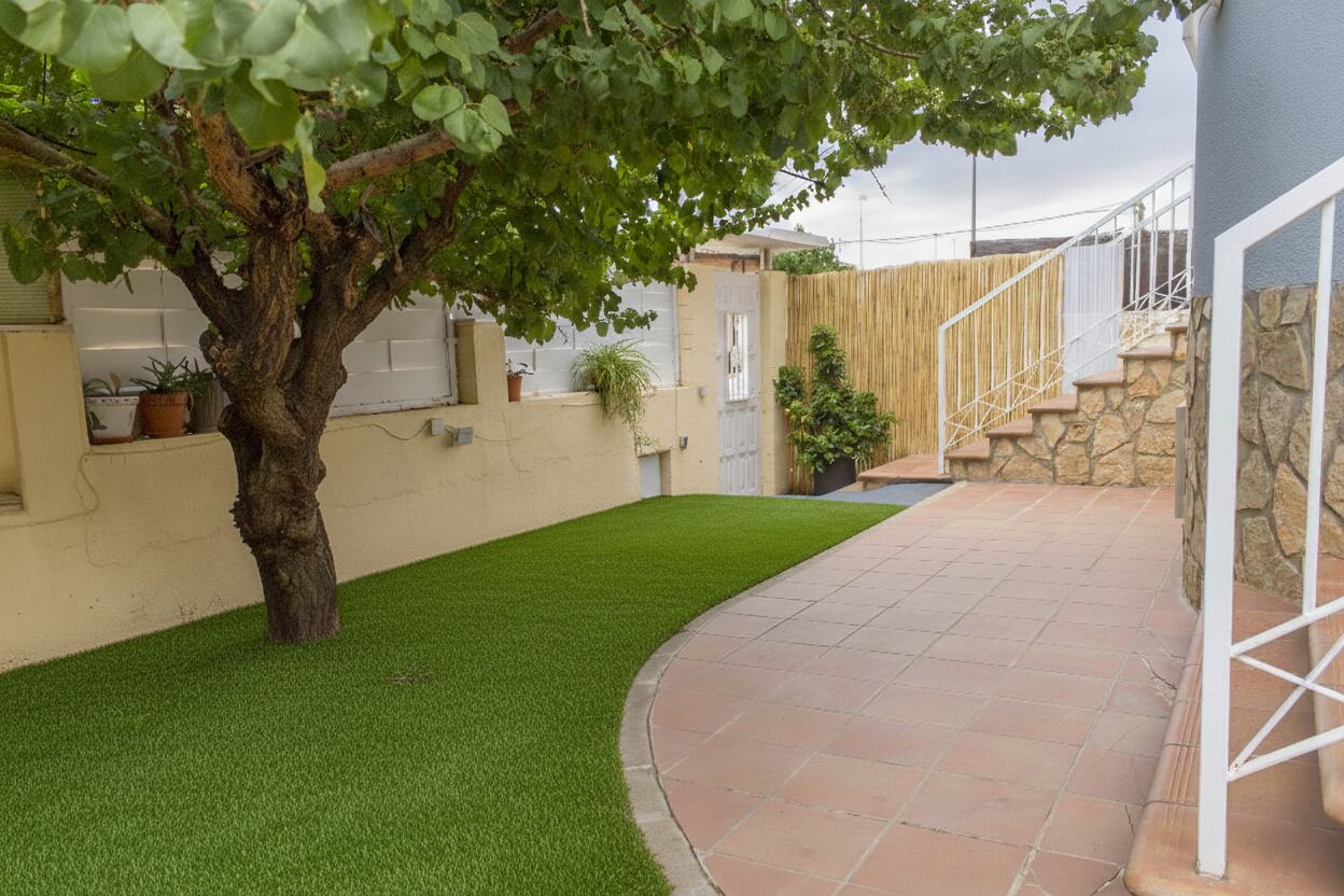 A courtyard with artificial grass, a tree, and a stone staircase leading to a white door.