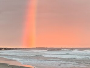 Uma praia com ondas e um arco-íris no céu.