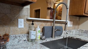 Una cocina con encimera de granito, pileta de acero inoxidable y salpicadero de losetas de piedra.