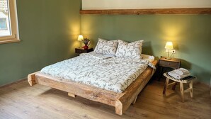 A wooden bed with floral bedding, two bedside lamps, and a small wooden stool with towels. - Pure relaxation: stylish nature retreat with sauna & chicken idyll (Hofheim in Unterfranken)