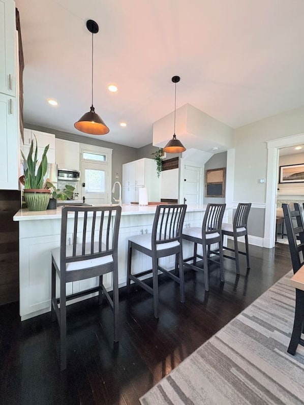 A modern kitchen with dark wood flooring, white cabinetry, and pendant lighting.