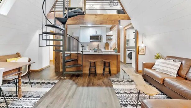 Eine Loft-Wohnung mit einer zentralen Küche, einer Wendeltreppe, einem Essbereich und einem Wohnzimmer mit Sofa und Couchtisch.