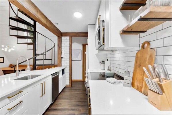 Una cocina moderna con armarios blancos, una escalera de madera y una tabla de cortar de madera.