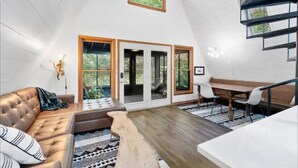 Ein geräumiger Loft mit hohen Decken, einer gemütlichen Sitzecke mit Sofa und Bank, einem Esstisch mit Stühlen und einer Treppe, die zu einer oberen Ebene führt.