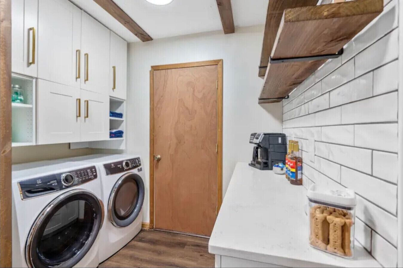 A compact kitchen with white cabinets, a wooden door, and a coffee machine on the counter.
