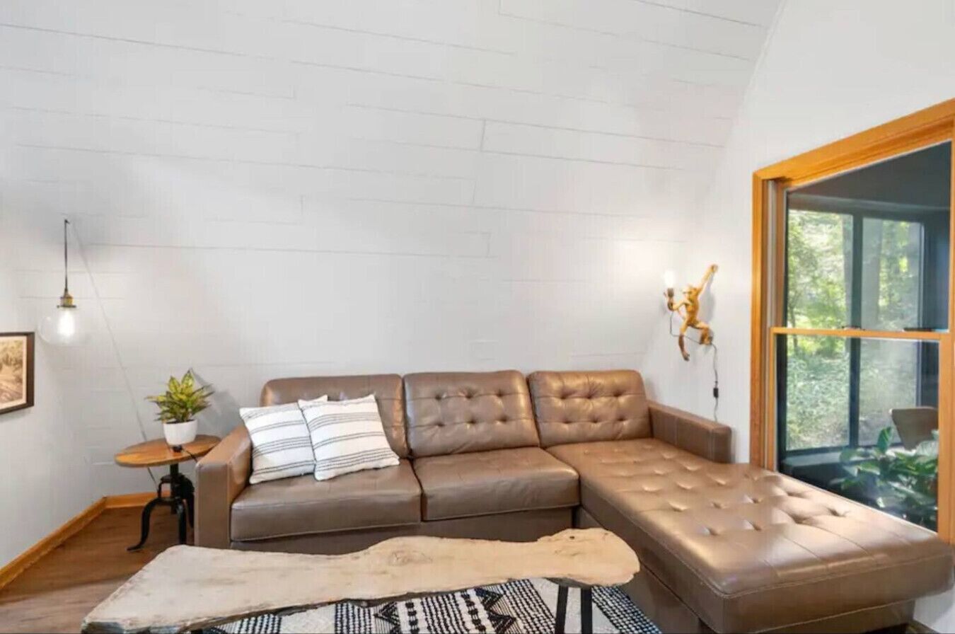 A modern living room with a sectional sofa, a small table with a plant, a rug, and a large window with a view of greenery.