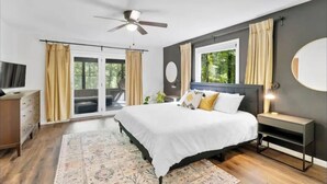Ein modernes Schlafzimmer mit Bett, Deckenventilator, Nachttisch und einem großen Fenster mit Vorhängen.