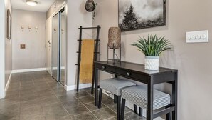 Un couloir avec une console en bois foncé, deux chaises à motifs, une plante suspendue, une décoration murale tissée et un tableau encadré accroché au mur.