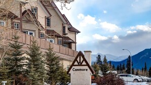 Un hôtel avec une enseigne indiquant « Canmore », entouré de neige, d’arbres et de montagnes en arrière-plan.