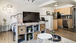 Une chambre moderne équipée d’un lit, d’une télévision et d’un meuble de rangement. On y trouve également un coin cuisine avec des placards en bois et un réfrigérateur.