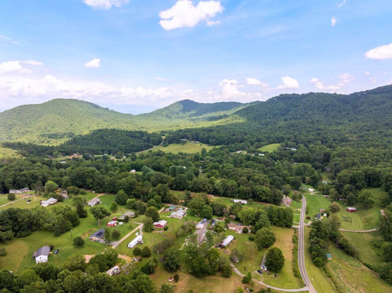 An aerial view of a rural area with scattered houses, roads, and green hills.
