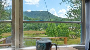 Vista desde una ventana con una taza sobre una mesa, mostrando un paisaje verde con árboles y una colina.