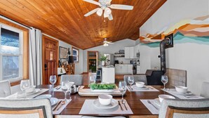 Un comedor con techo de madera, vista a la cocina y una mesa de comedor con platos, vasos y cubiertos.