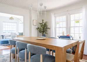 Et spiseområde med et træbord, fire grå stole, en vase med grønne planter og en loftventilator.