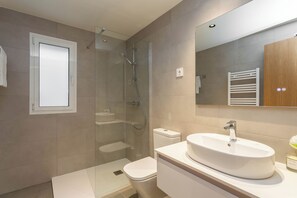 Et moderne badeværelse med en glasafskærmet brusekabine, en hvid vask og et trækommode.