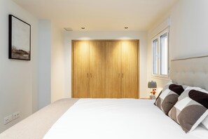 A bedroom with a bed, a wooden wardrobe, a nightstand with a lamp, and a window. - Enjoy a comfortable and modern stay in this bright apartment located on the fifth floor of a building with an elevator, on the central Félix Boix street and just a 5-minute walk from Plaza de Castilla. (MADRID)