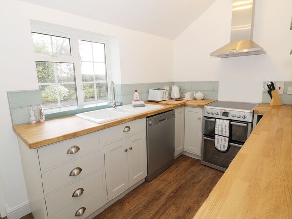 A modern kitchen with a dishwasher, oven, and a window with a view of greenery. - Glencoe Cottage (Broadway)
