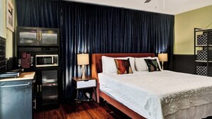 A hotel room with a bed, a desk with a microwave, a small cabinet, and a ceiling fan. - Rainbow Falls 2 Stay for 2 (Oakland Park)