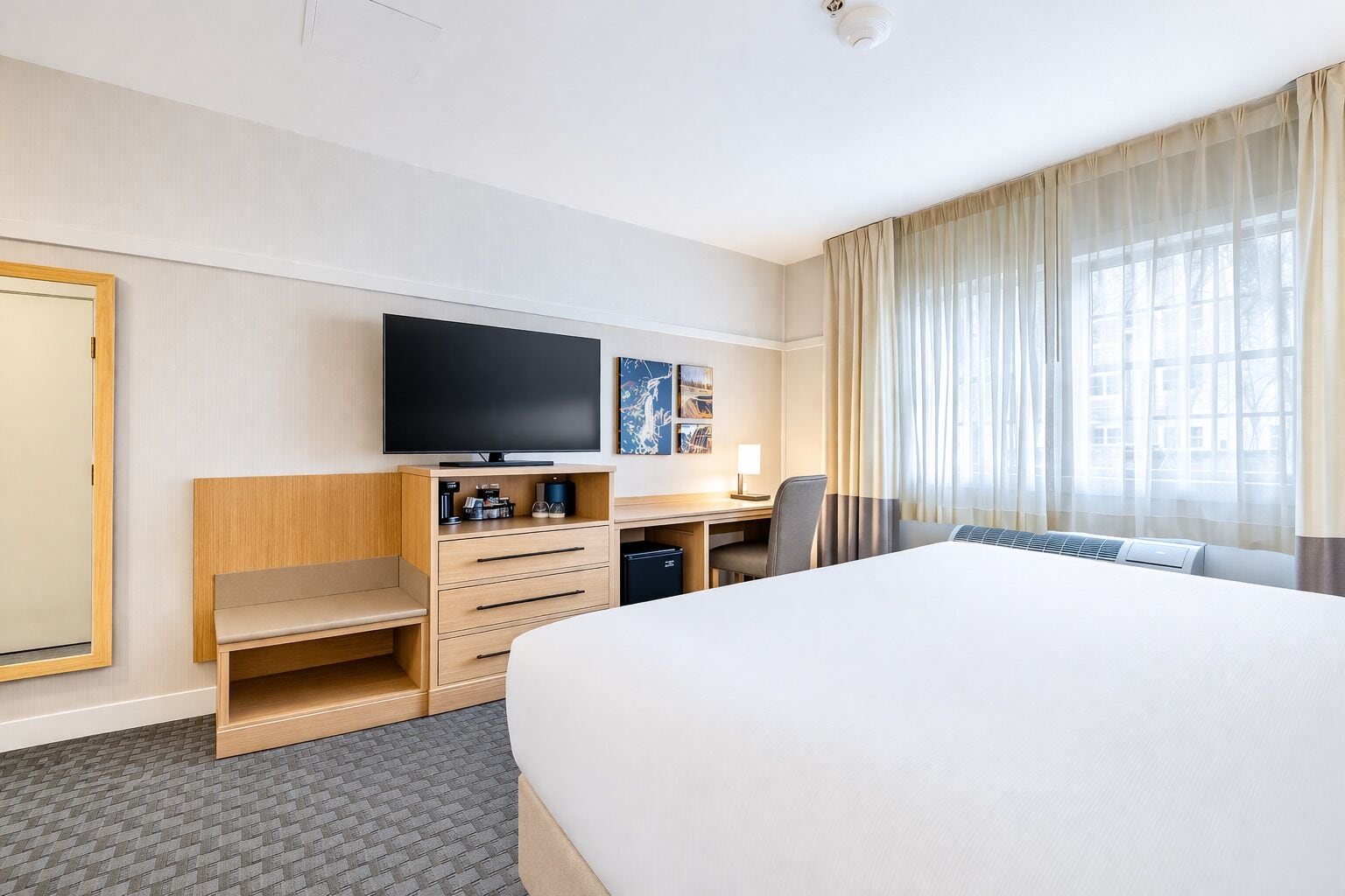 A hotel room with a large bed, a desk with a chair, a television, and a window with curtains.