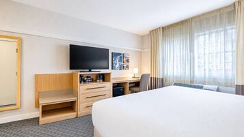 A hotel room with a large bed, a desk with a chair, a television, and a window with curtains.