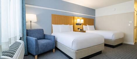 Quarto de hotel com duas camas, uma poltrona azul, um aquecedor e uma mesa de cabeceira com luminárias.