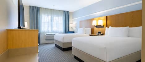 Ein Hotelzimmer mit zwei Betten, einem Fernseher, einem Schreibtisch und einem Fenster mit Vorhängen.