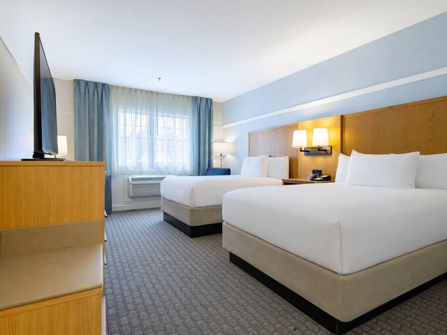 Habitación de hotel con dos camas, televisión, escritorio y ventana con cortinas.