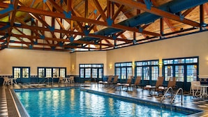 Una piscina con plataforma de baldosas, sillas de descanso y techo alto con vigas de madera.