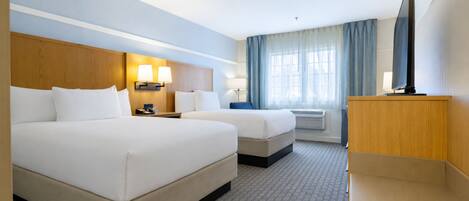A hotel room with two beds, a TV, a desk, and a window with curtains.