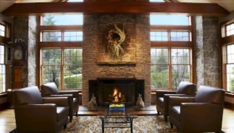 A spacious room with a stone fireplace, large windows, and leather armchairs.