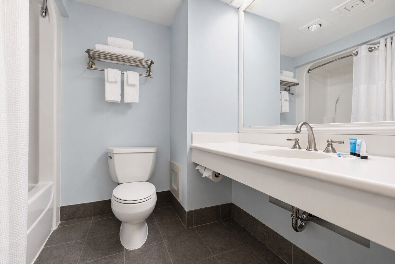 A modern bathroom with a toilet, a sink with a mirror, and a towel rack.