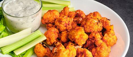 A plate of seasoned cauliflower with celery and a glass of ranch dressing.