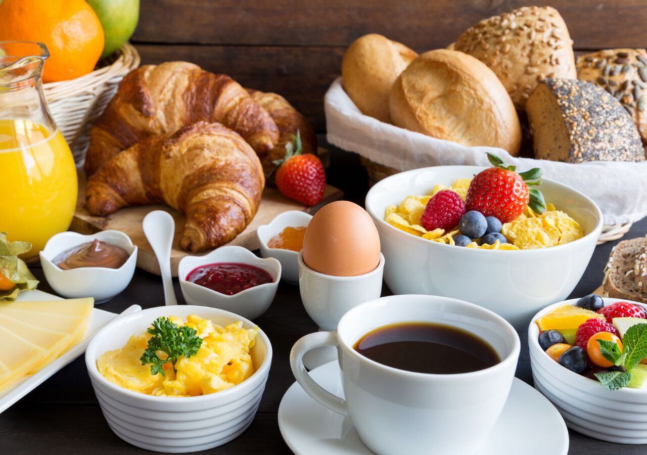 Colazione con croissant, pane, uova, frutta e caffè.
