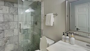 Ett badrum med en dusch som är avskärmad med glasväggar, en toalett, ett handfat med hygienartiklar och en spegel.