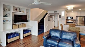 Un salon moderne avec un canapé en cuir bleu, un téléviseur à écran plat et un escalier menant à un espace cuisine.