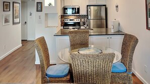 Une cuisine moderne avec des meubles blancs, des appareils en acier inoxydable et une table à manger en verre, accompagnée de chaises en osier.