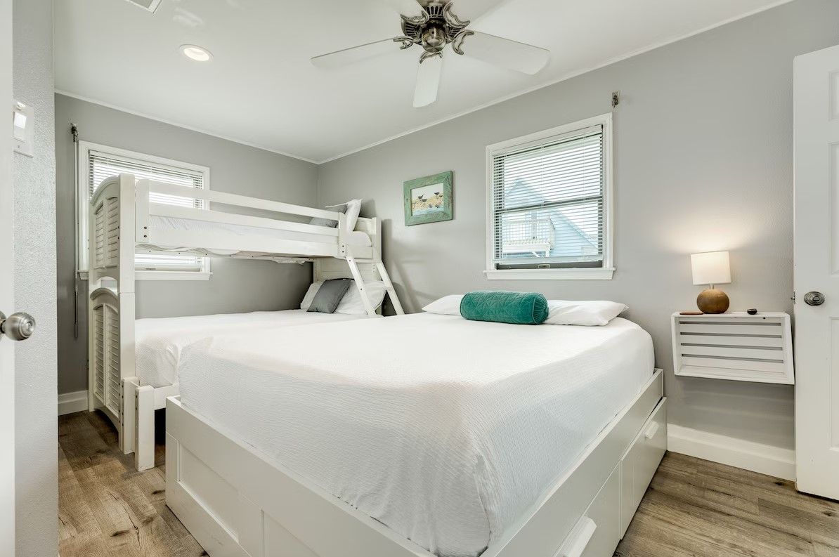 A bedroom with a bunk bed, a bedside table, a lamp, and a window with blinds.
