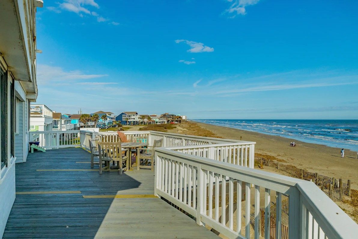 Eine Holzterrasse mit weißen Geländern mit Blick auf einen Strand.