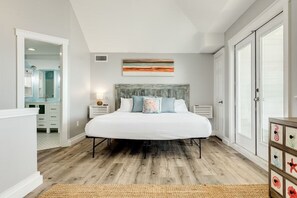 A bedroom with a large bed, a headboard, a nightstand, a dresser, and a window with blinds. - Oceanfront Vista (Galveston)